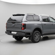 Gray Ford Ranger truck with a hard lid parked in front of a gray building.