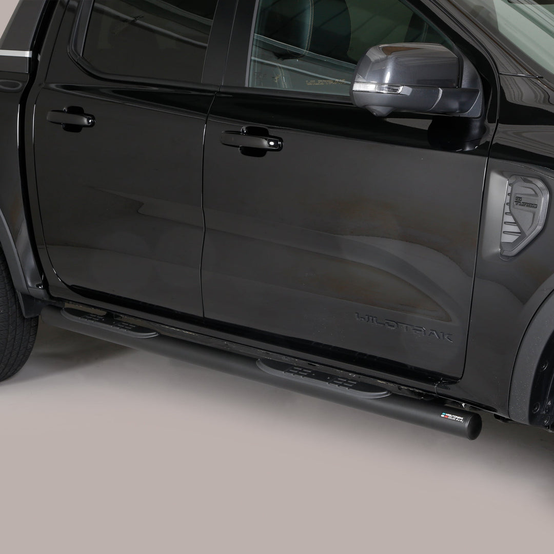 A black side step bar installed on the rear side of a black pickup truck, shown in a studio setting against a light gray background.