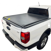 A black roll-up truck bed cover installed on a white pickup truck, shown from the rear three-quarter angle. The product is displayed on a white background within a website or app interface, with a smartphone app screen and a key fob shown as included accessories.