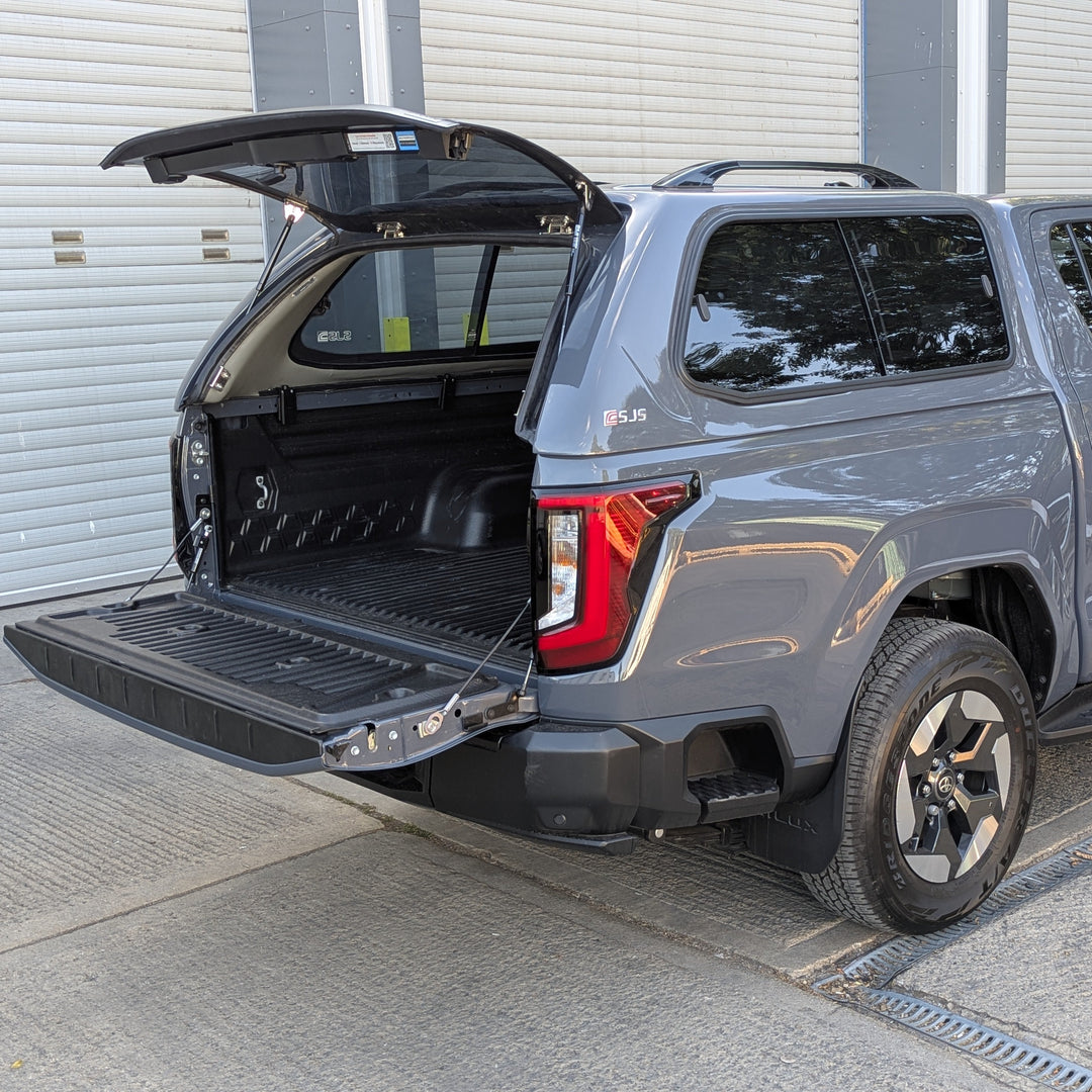 A gray pickup truck with a rear cargo bed and open tailgate, parked outdoors in front of a white garage door.
