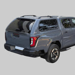 Load image into Gallery viewer, A dark gray pickup truck Travo with a hardtop canopy and black wheels, photographed from the rear three-quarter angle in an outdoor driveway in front of gray garage doors.