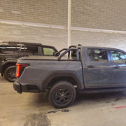 A dark gray pickup truck parked inside a warehouse or garage. The truck has black wheels, a black bed roll, and a tonneau cover.
