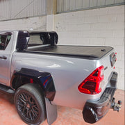 A silver Toyota Hilux pickup truck with black custom body kits, flared wheels, and a black tonneau cover, parked inside.