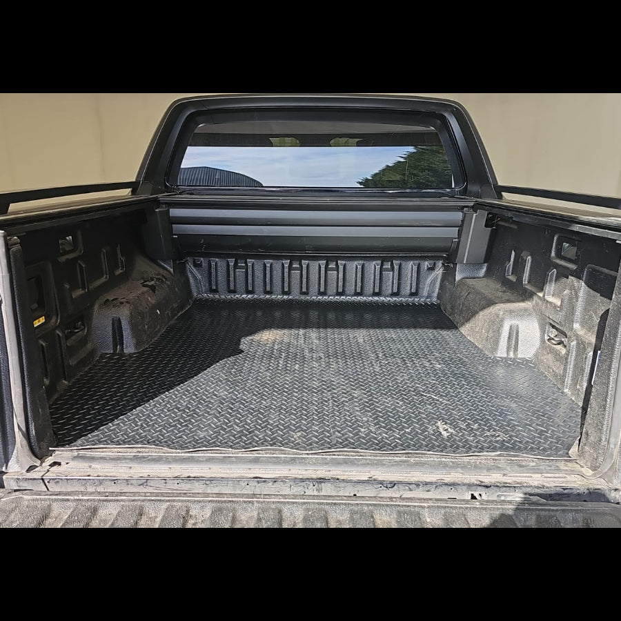 A black textured diamond-plate style truck bed liner installed inside the bed of a pickup truck, shown from the rear with the tailgate open.