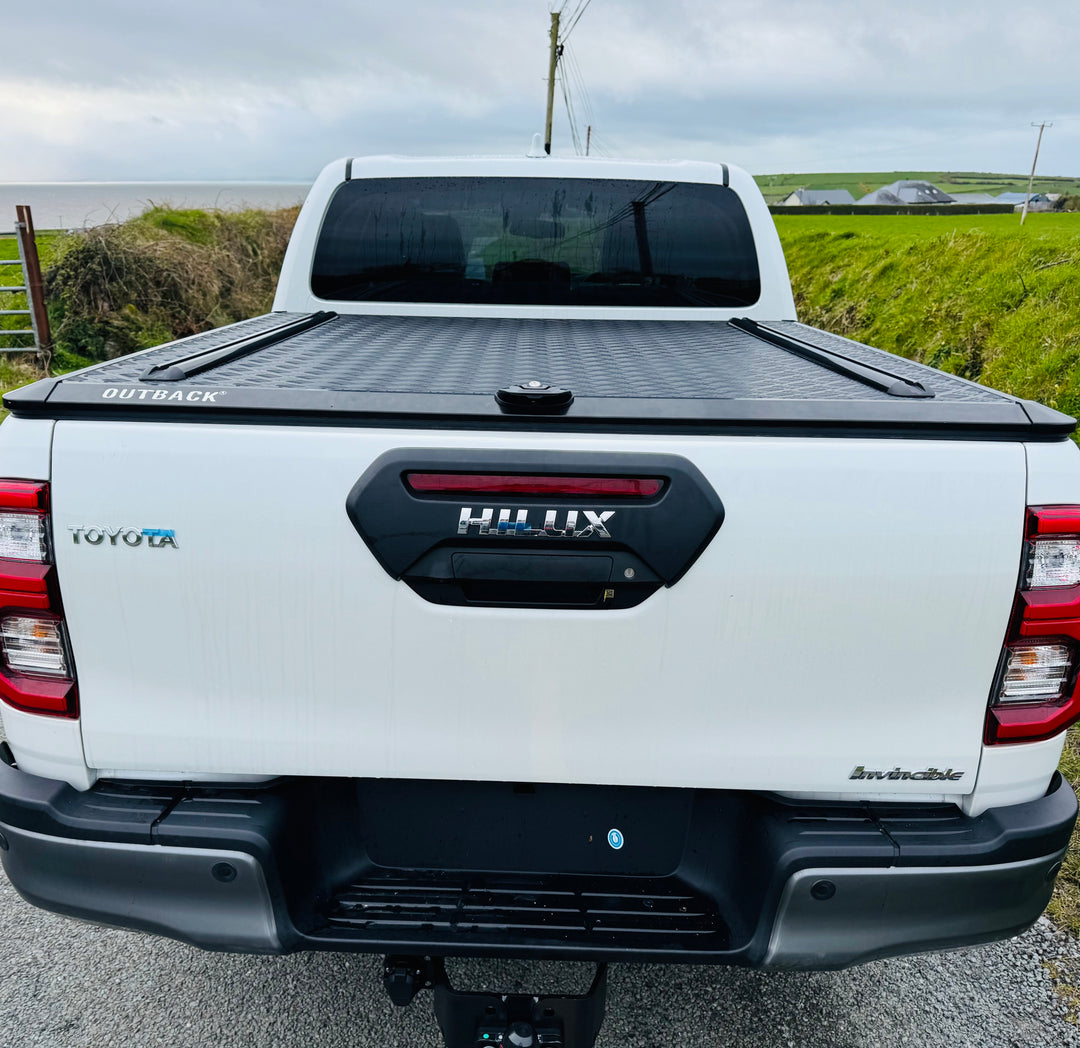 Toyota Hilux truck with a black tonneau cover on a road.