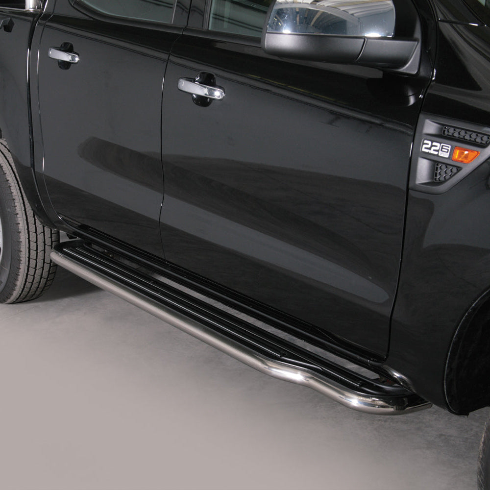 A close-up side view of a black pickup truck showing a long chrome side step running along the lower door, with part of the rear wheel and front wheel visible against a plain light gray studio background.