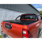 Load image into Gallery viewer, A black Interceptor roll-up truck bed cover installed on the bed of an orange pickup truck Revo, photographed outdoors next to a gray building.