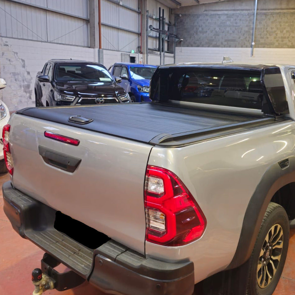 A silver pickup truck Toyota Hilux with a black tonneau cover roller shutter
